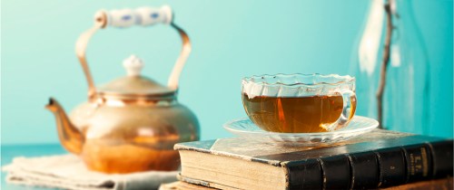 Cup of tea with teapot and vintage books on wooden table Blue background